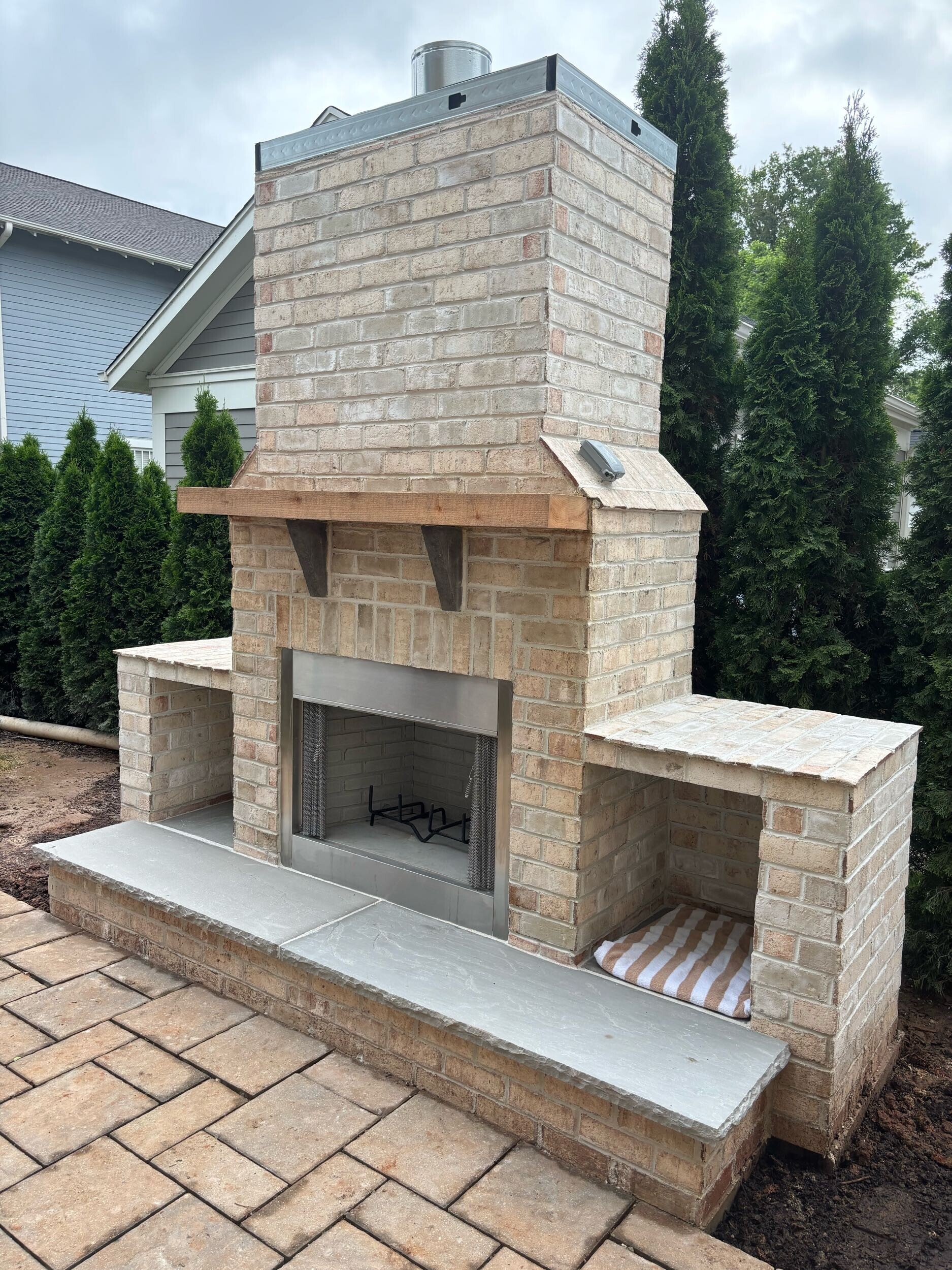 A newly built brick and stone outdoor fireplace on a paver patio.